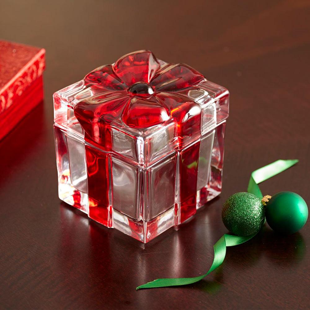 Clear glass cube gift box with red contents and a flower shaped lid on a dark wooden surface