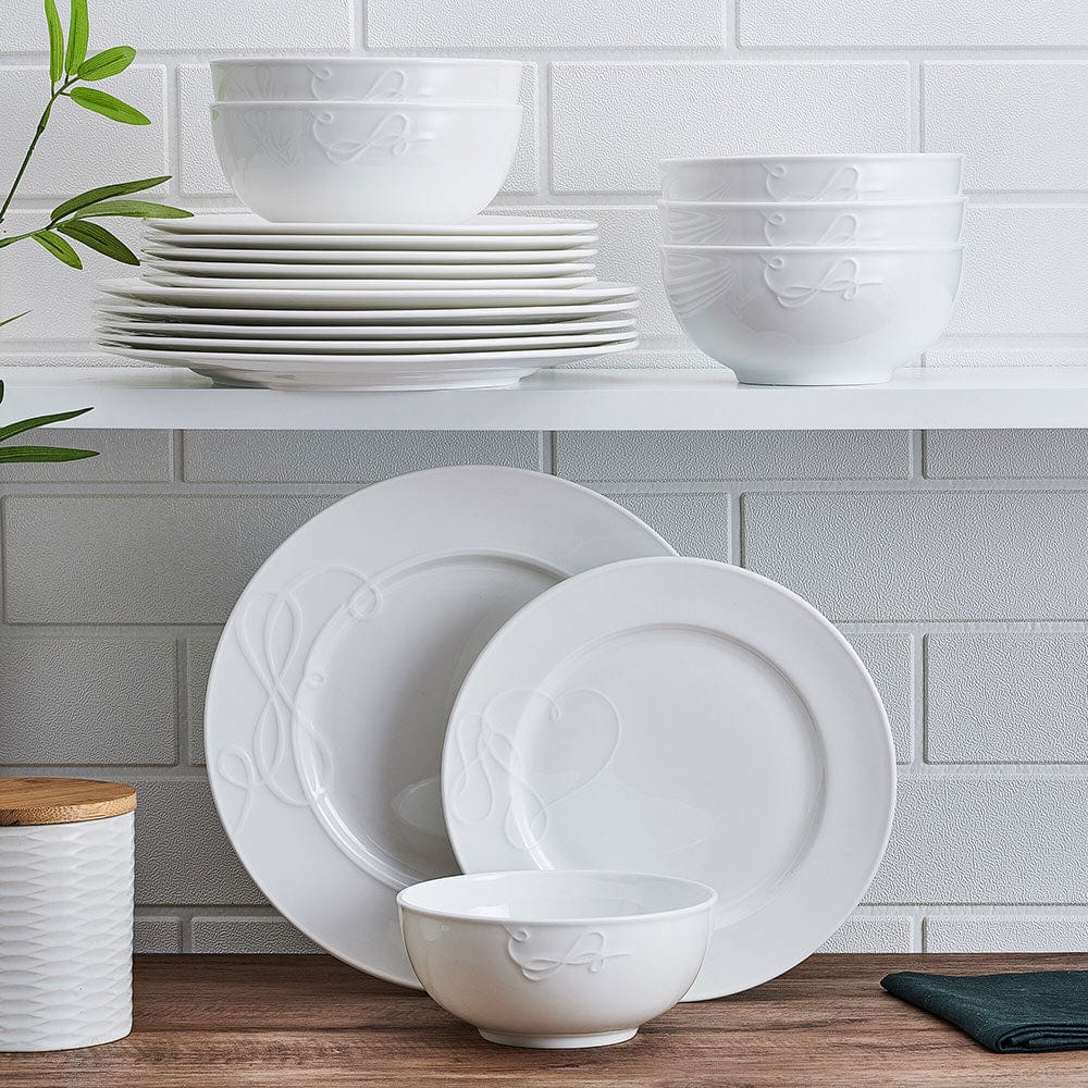 Love Story white embossed dinnerware bowls and plates stacked on a shelf against a white brick wall