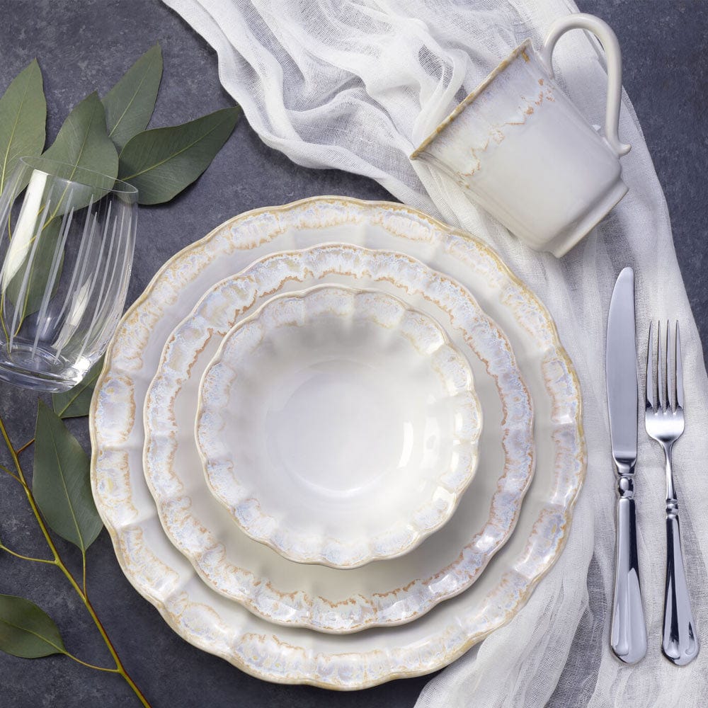 Mila four piece place setting with layered cream plates and silverware on a dark surface