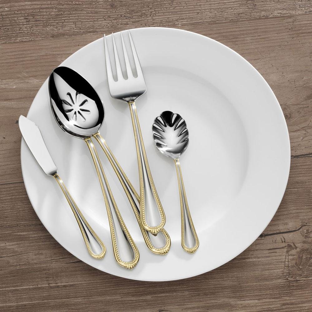 Regent Bead Gold flatware with beaded handles arranged on a white dinner plate on a wooden table.