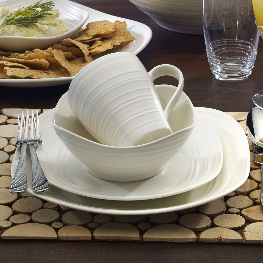 White swirl dinnerware place setting with a mug inside a bowl atop a plate on a wooden table