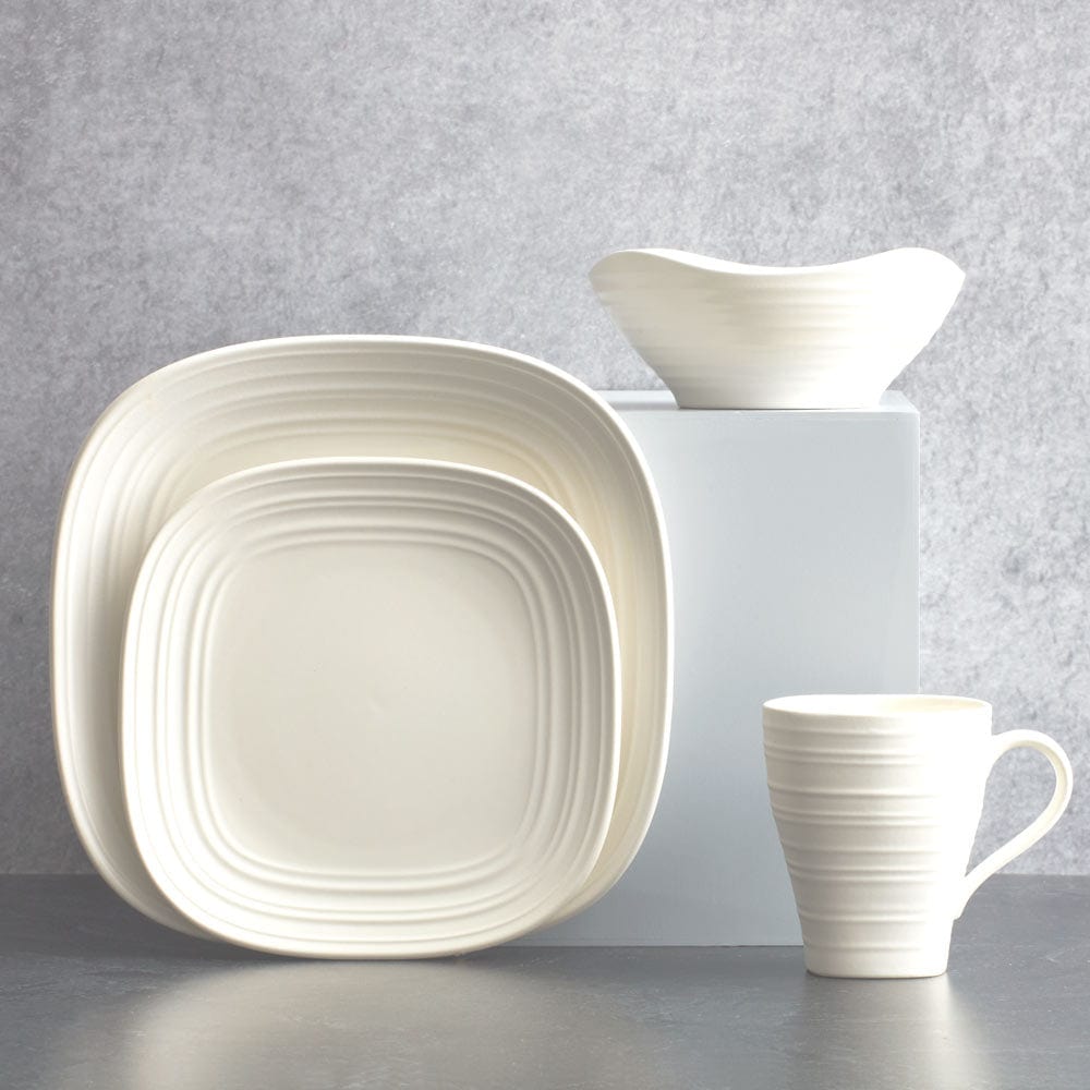 Stacked square plates with ridged edges along with a mug and a small bowl from the Swirl White Square dinnerware set.