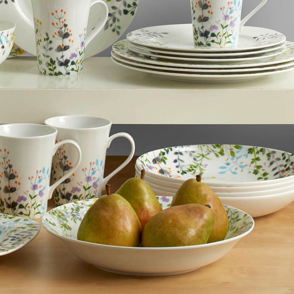 Tivoli Garden dinnerware set with plates mugs and a bowl arranged on a table beside fresh pears.