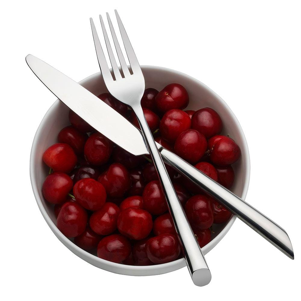 White bowl filled with cherries with two crossed forks and a knife resting across them